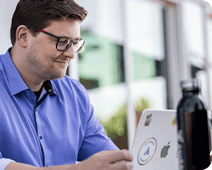 Focused team member working outdoors on a sticker-covered laptop next to a reusable water bottle.
