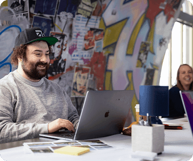 Developer smiling while working on a laptop in a vibrant, creative workspace with a graffiti-covered wall.